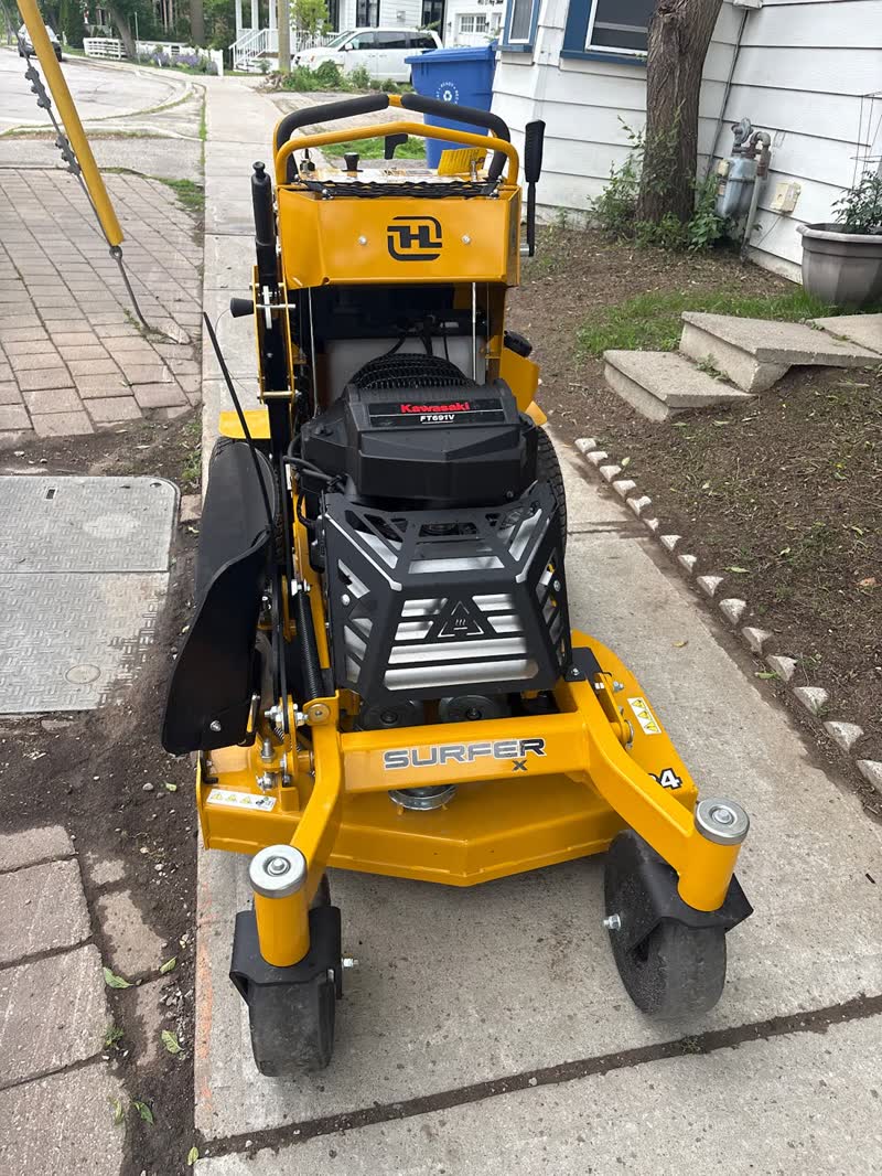A Hustler Surfer X stand-on mower parked on a driveway